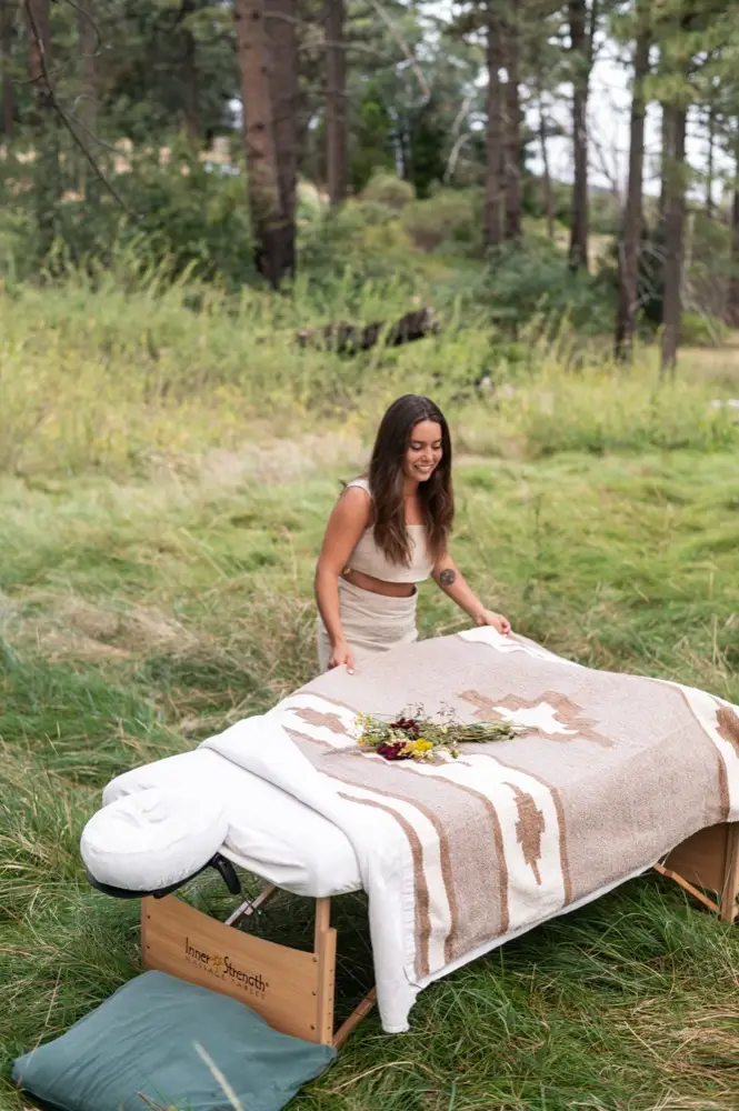 Katrinna Jasso preparing her massage table with flowers in a forest meadow